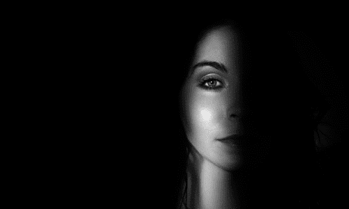 Foto a preto e branco de mulher na sombra com um feixe de luz a iluminar parte da cara